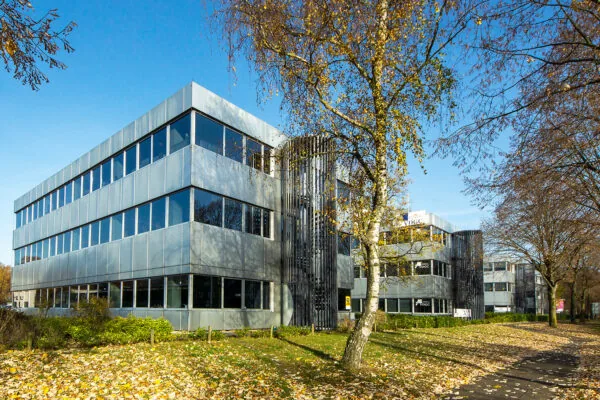 Modern kantoorgebouw aan de Huis ter Heideweg omgeven door herfstbomen en vallende bladeren.